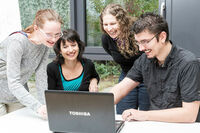 four smiling persons together looking at a laptop